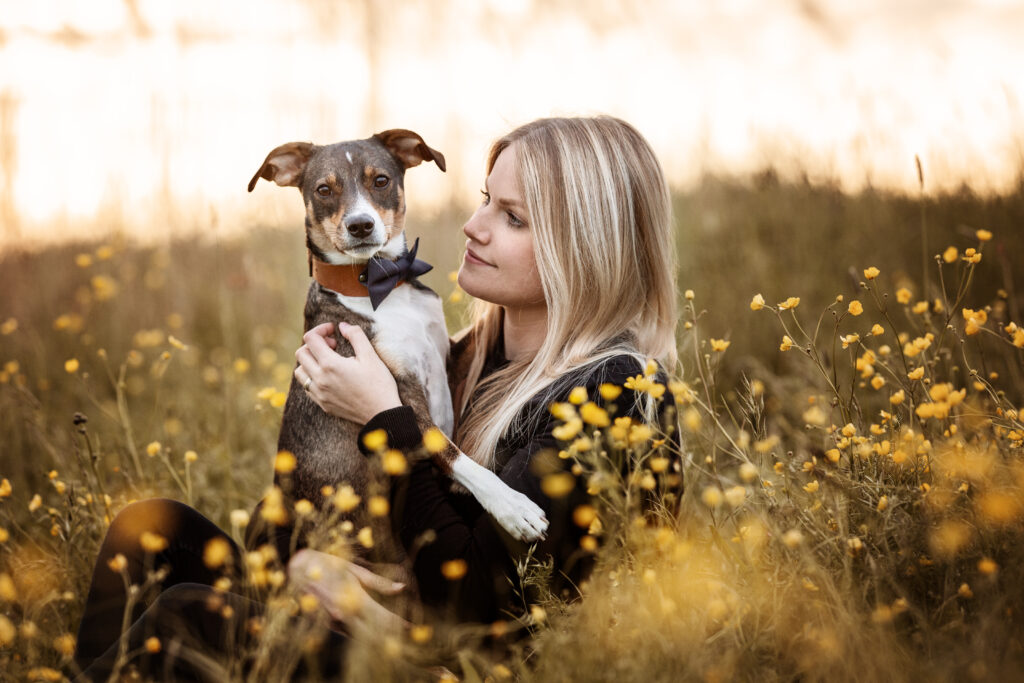 Frau und Hund kuscheln in einer Blumenwiese bei Hundefotoshooting mit Coralie Duda Fotografie im Wetteraukreis