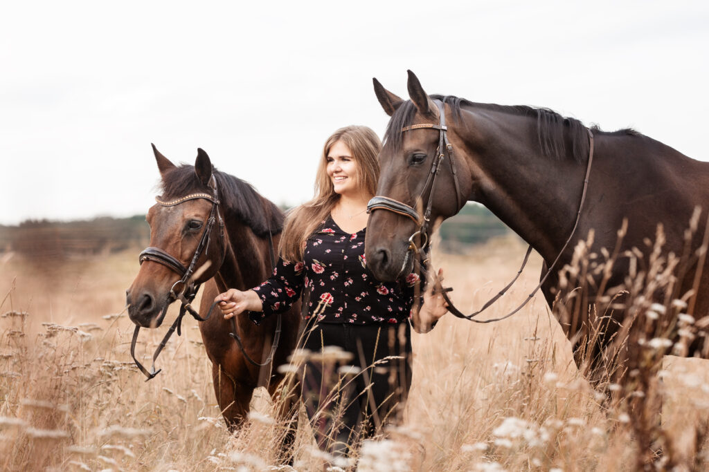 Frau mit Pferden in einer Blumenwiese bei Fotoshooting mit Coralie Duda Fotografie im Wetteraukreis